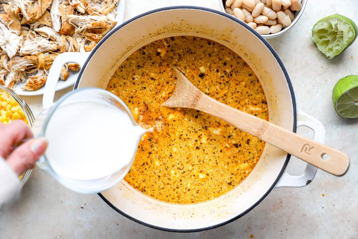 Half and half being poured into the chili base to create a creamy white chicken chili broth