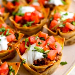 Taco cups made with wonton wrappers topped with sour cream, diced tomatoes, and cilantro