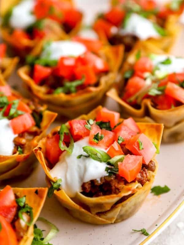 Taco cups made with wonton wrappers topped with sour cream, diced tomatoes, and cilantro