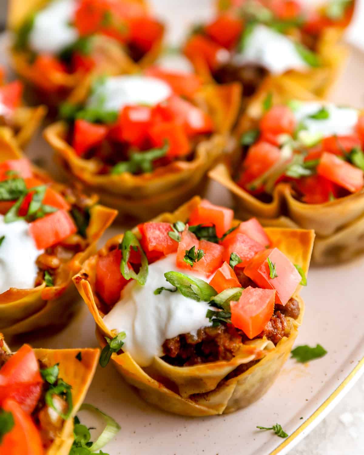 Taco cups made with wonton wrappers topped with sour cream, diced tomatoes, and cilantro
