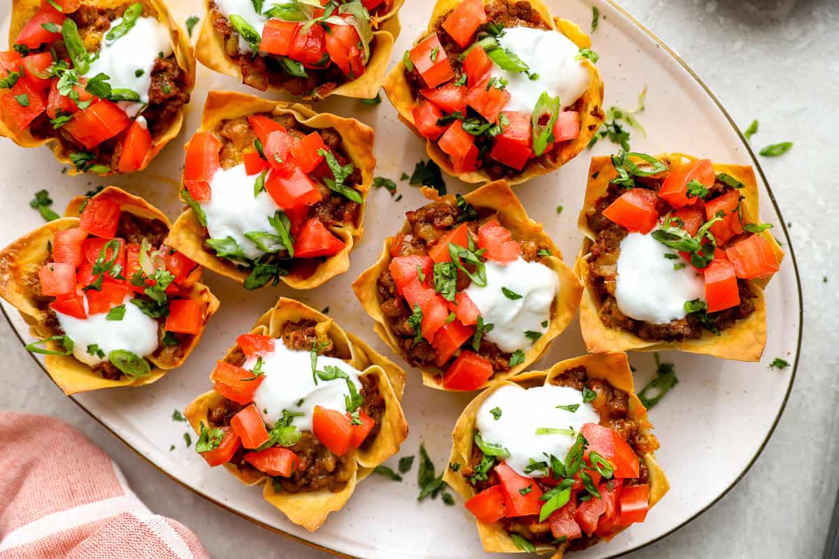 Crispy taco cups topped with sour cream, diced tomatoes, and herbs on a serving platter