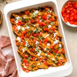 Taco stuffed shells baked in a casserole dish topped with diced tomatoes, sour cream, green onions, and cilantro.