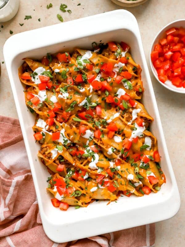 Taco stuffed shells baked in a casserole dish topped with diced tomatoes, sour cream, green onions, and cilantro.
