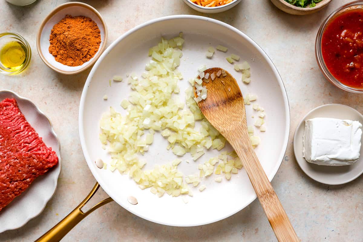 Chopped onions sautéing in a skillet with olive oil for taco stuffed shells filling.