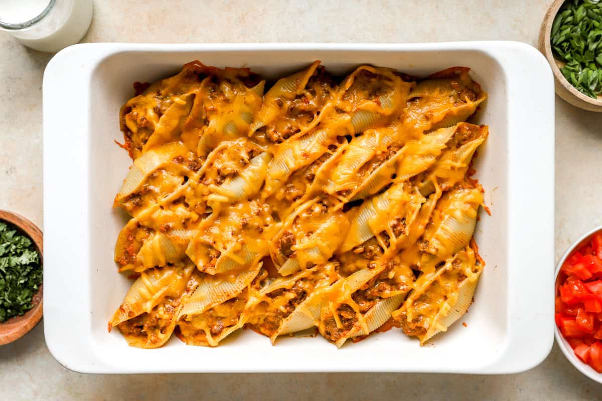 Baked taco stuffed shells with melted cheddar cheese in a white casserole dish.