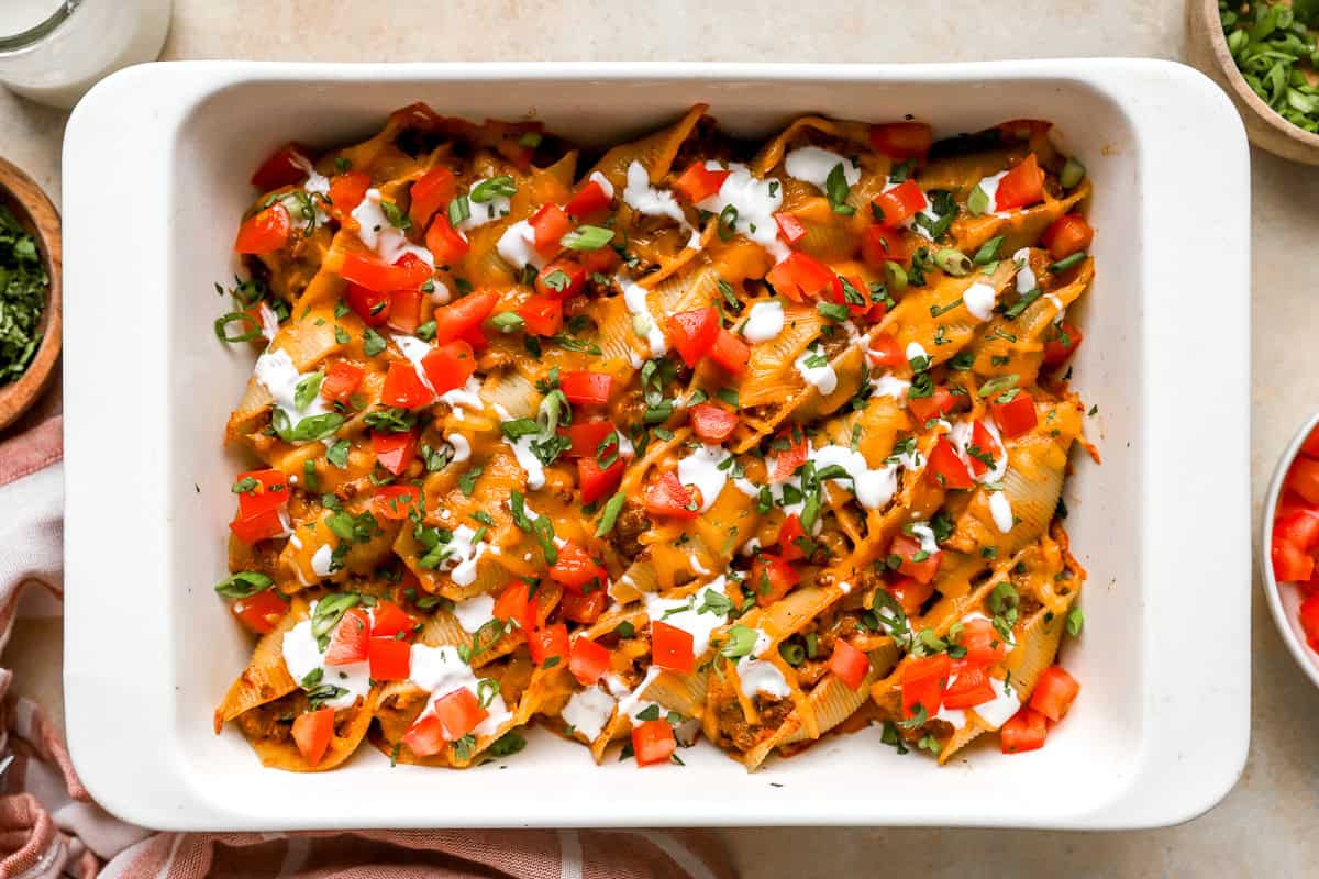 Taco stuffed shells topped with diced tomatoes, cilantro, green onions, and sour cream.