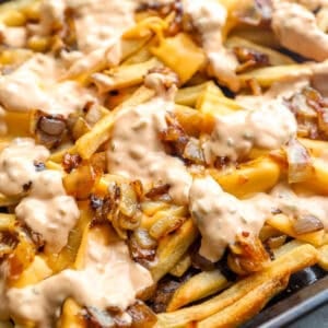 Animal style fries topped with melted American cheese, caramelized onions, and creamy sauce on a sheet pan