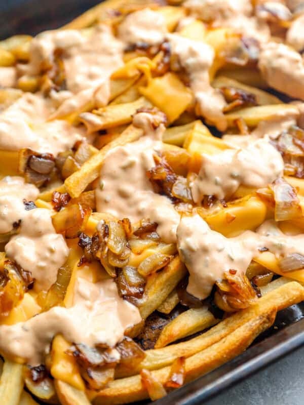 Animal style fries topped with melted American cheese, caramelized onions, and creamy sauce on a sheet pan