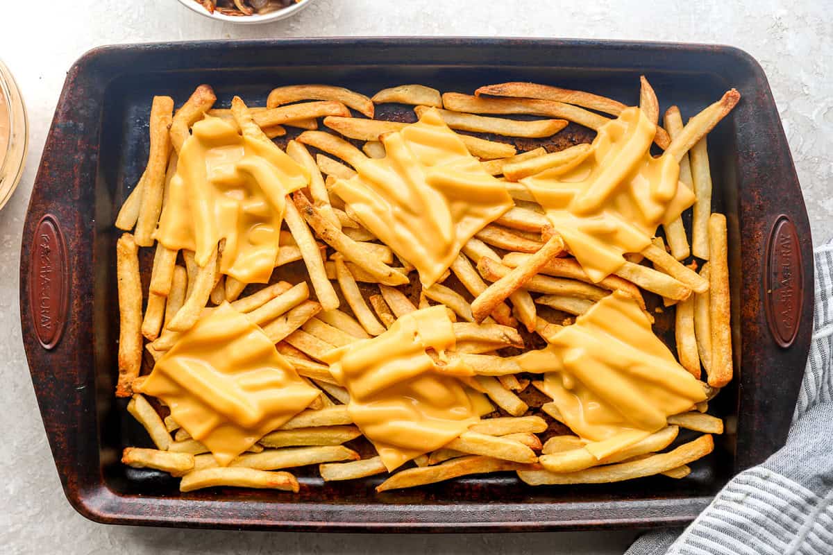 French fries topped with slices of American cheese ready to melt in the oven