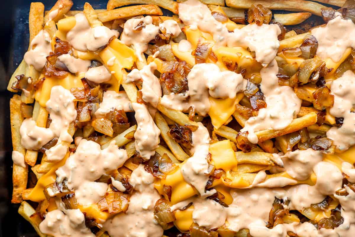 Sheet pan of animal style fries fully assembled with cheese, caramelized onions, and sauce ready to serve