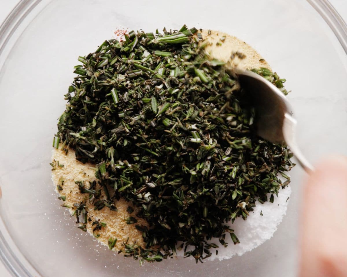 Close-up of a spice blend with chopped fresh herbs, paprika, salt, and garlic powder being mixed in a bowl.