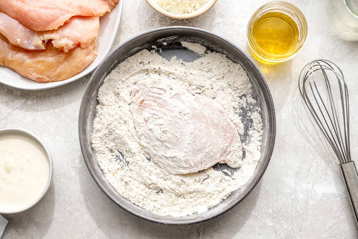Raw chicken breast dredged in seasoned flour mixture in a shallow bowl