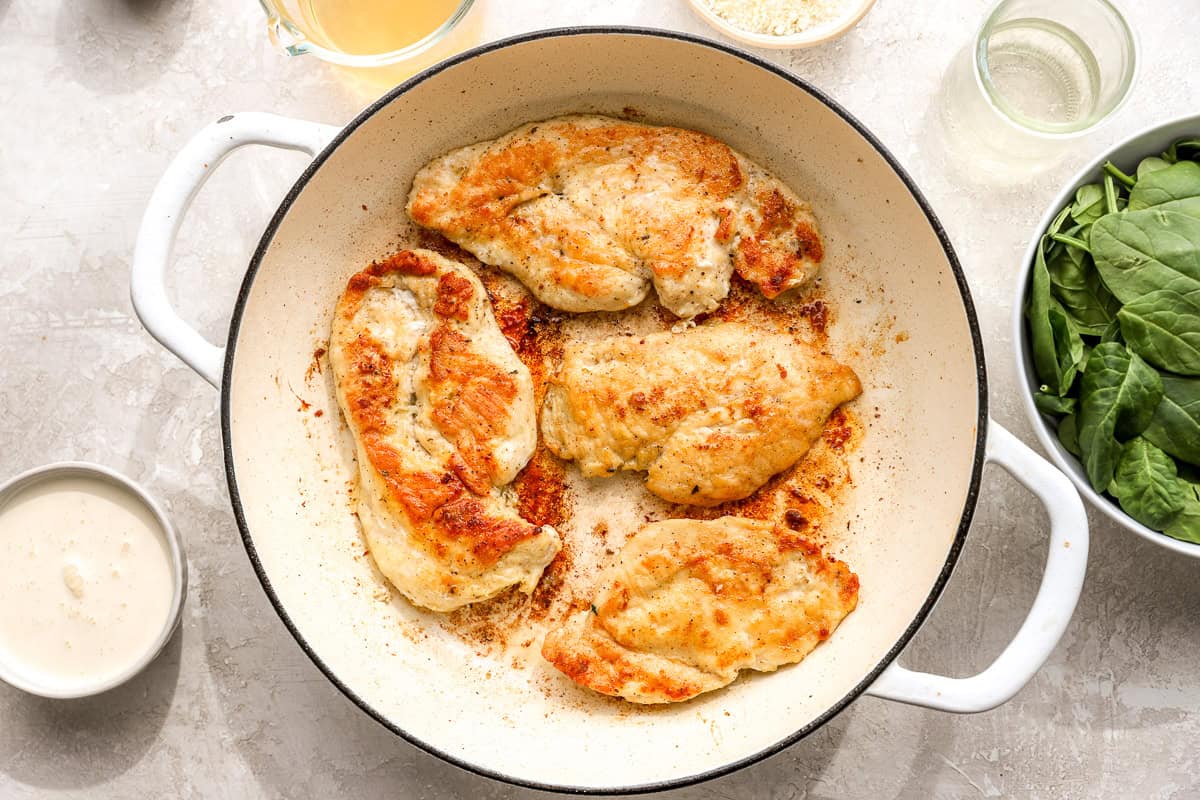Thin chicken breasts searing in a skillet until golden brown