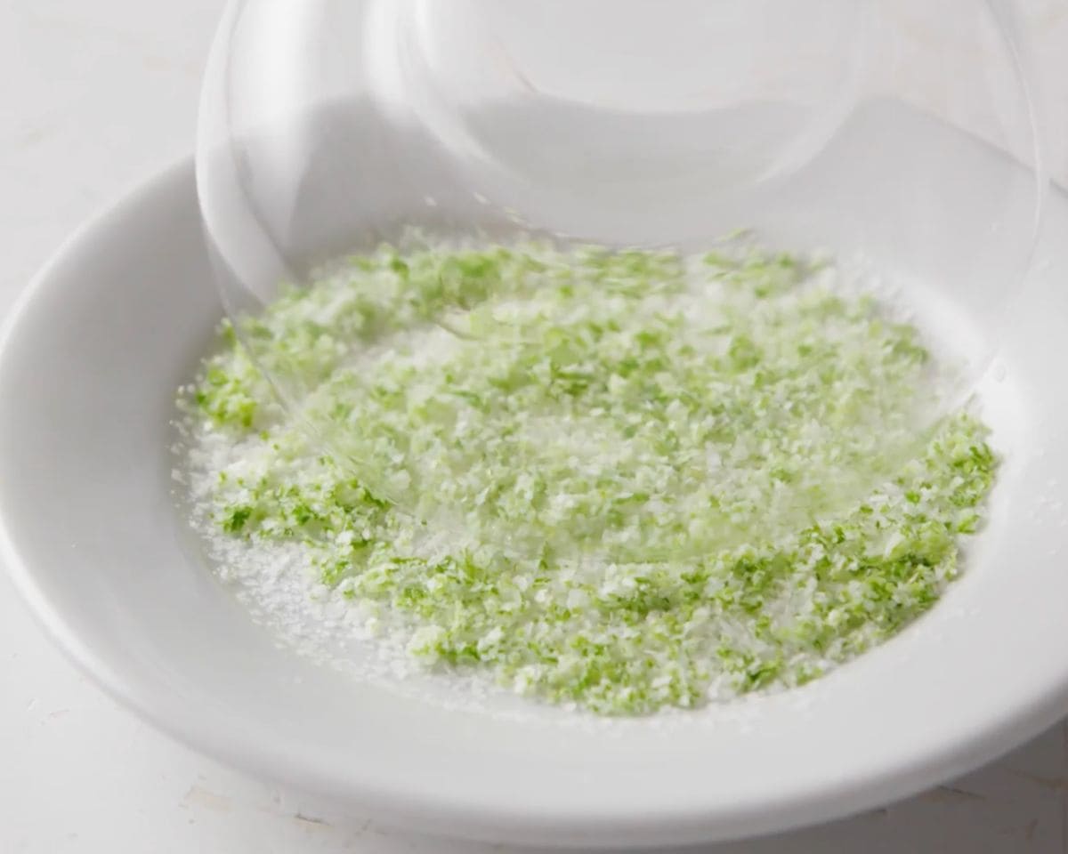 Margarita glass being dipped into a lime zest, salt, and sugar mixture for the rim.