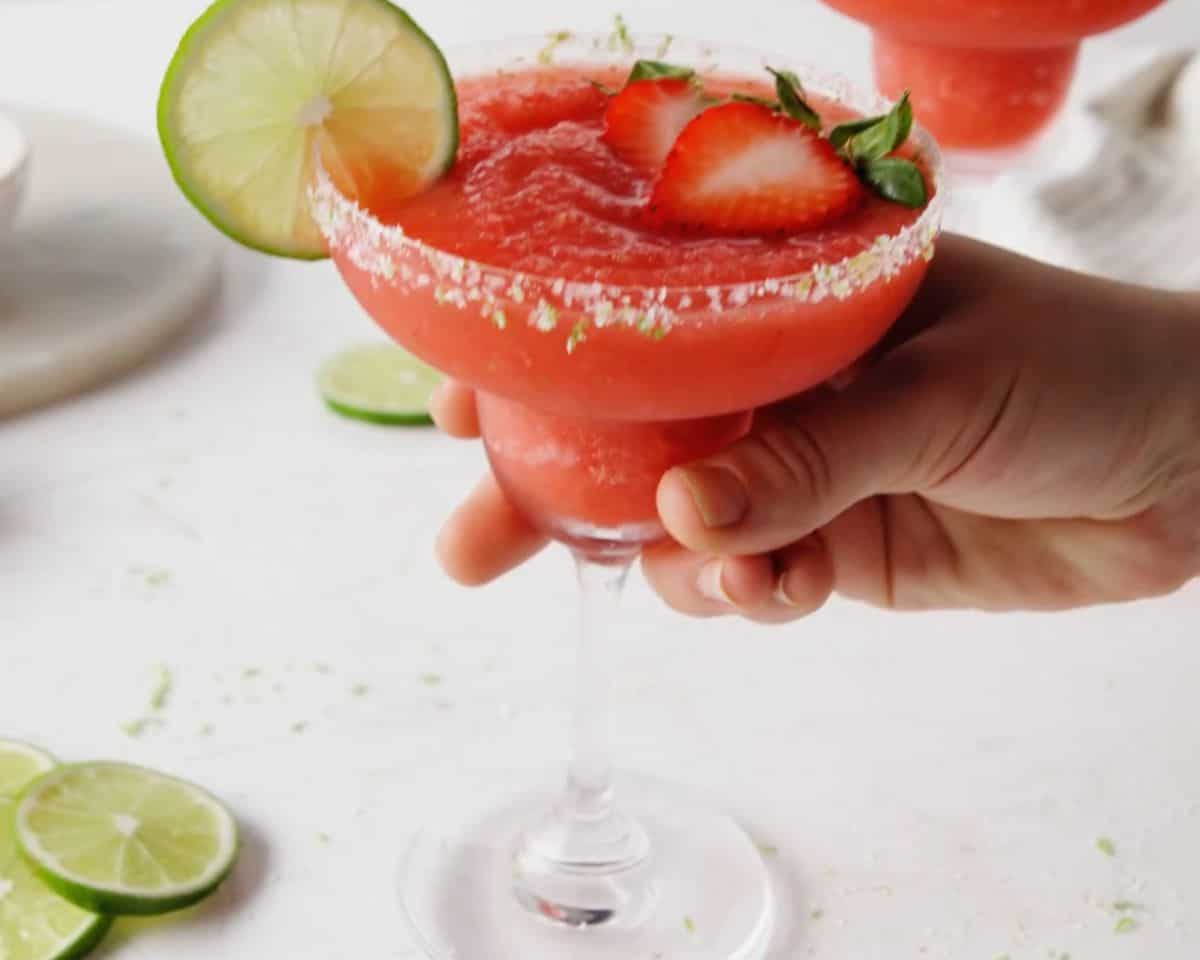 Frozen strawberry margarita garnished with fresh strawberries and a lime wedge in a margarita glass.
