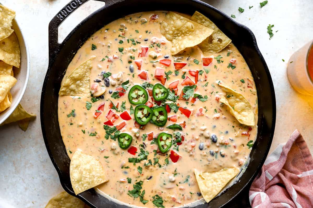Loaded cowboy queso finished with toppings in a skillet and tortilla chips on the side