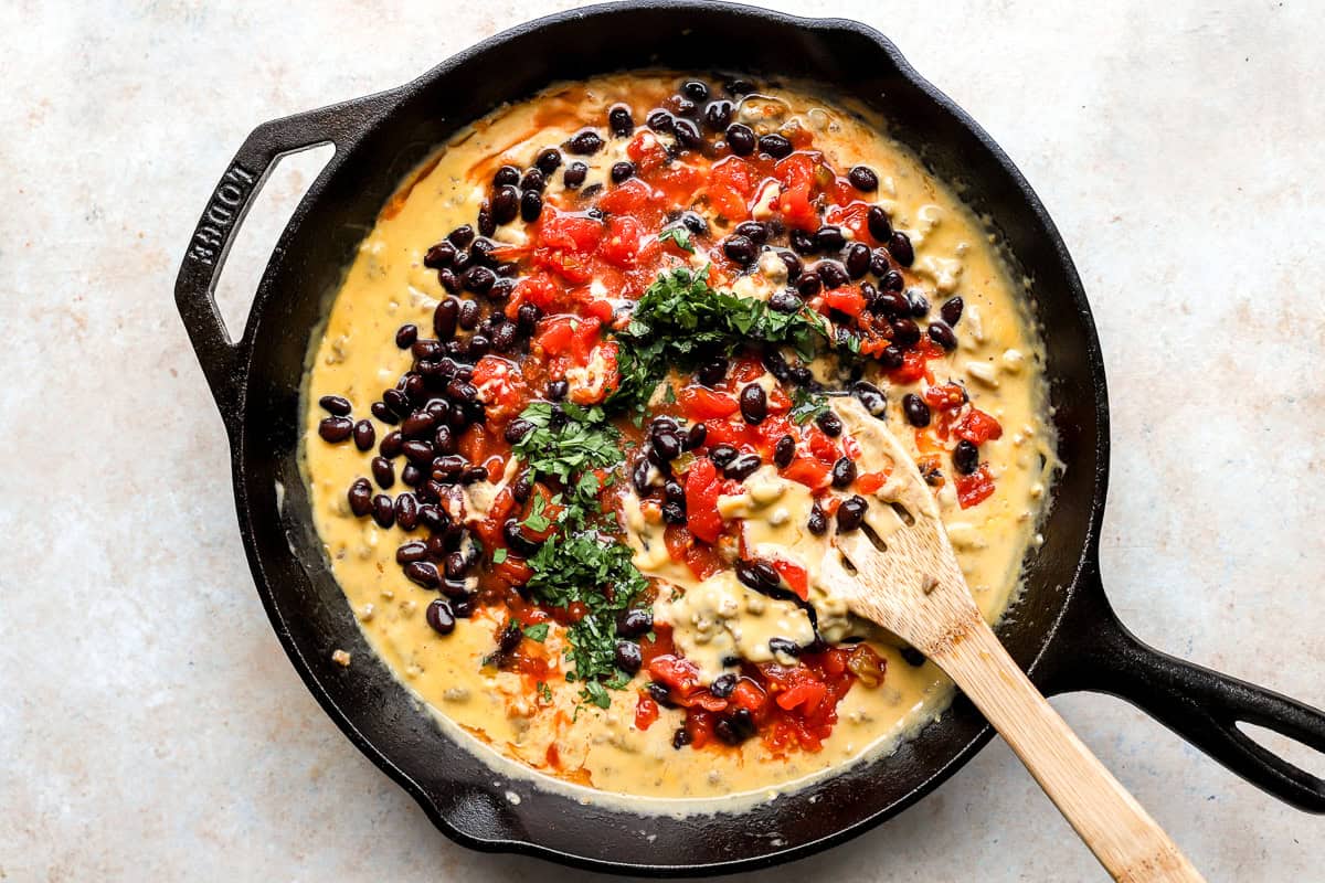 Adding black beans, Rotel tomatoes, and cilantro to melted cheese and sausage mixture in a skillet