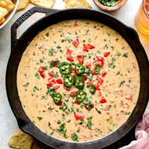 Loaded cowboy queso in a cast iron skillet topped with jalapeños, diced tomatoes, and fresh cilantro