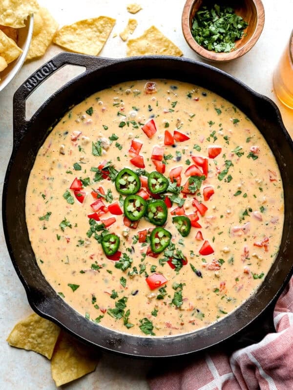 Loaded cowboy queso in a cast iron skillet topped with jalapeños, diced tomatoes, and fresh cilantro