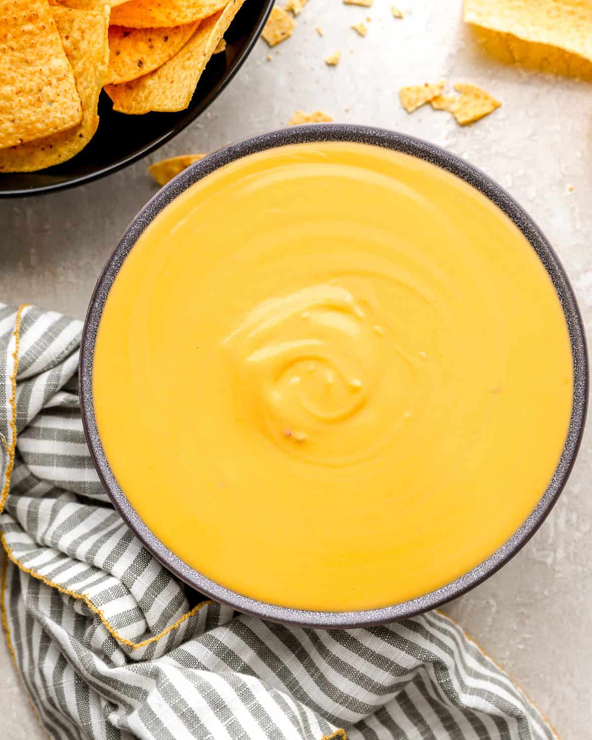 Smooth, creamy nacho cheese sauce in a bowl with tortilla chips on the side.