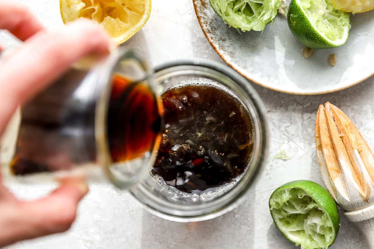 Pouring homemade ponzu sauce into a jar with fresh citrus and juicer in the background