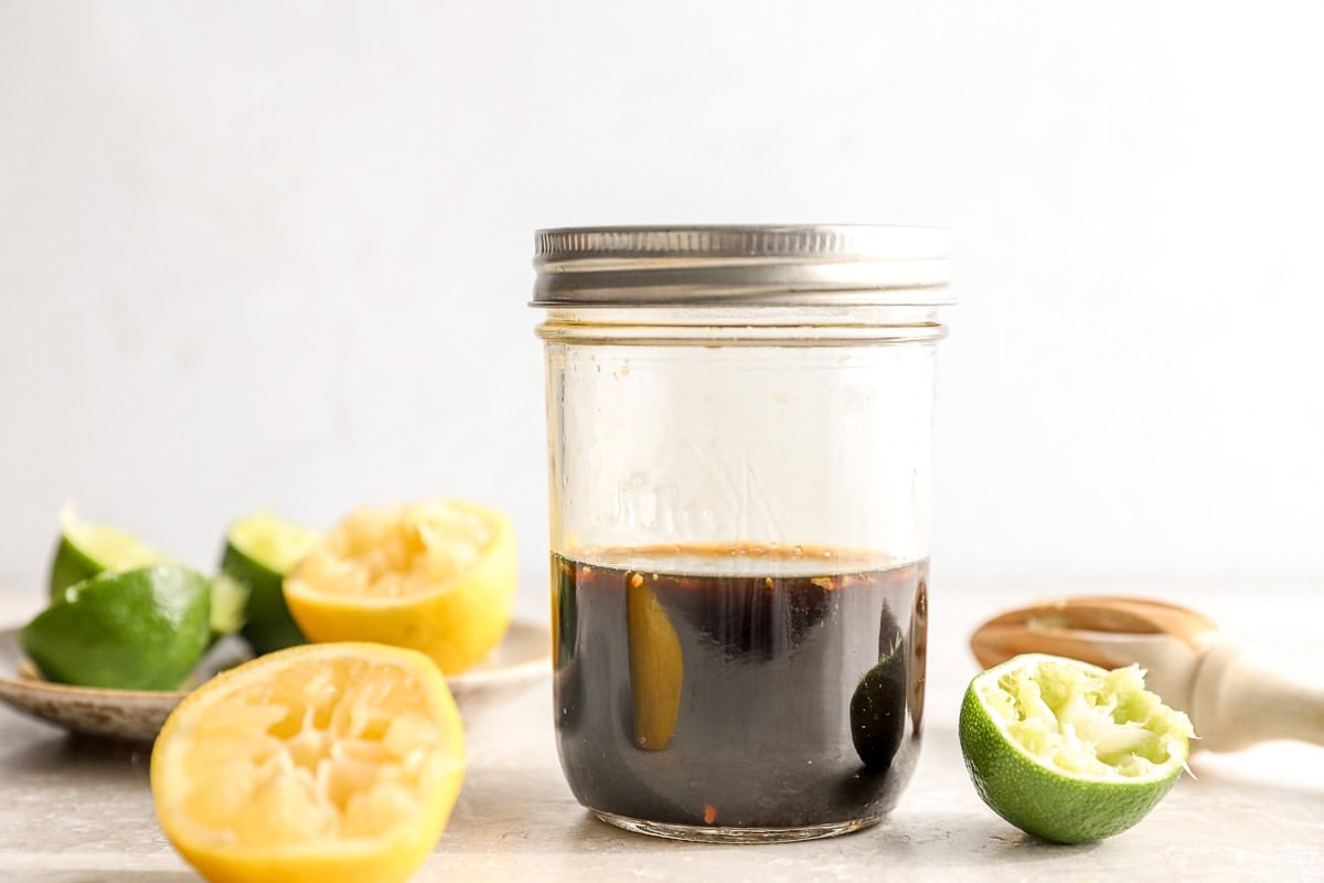 Glass jar filled with ponzu sauce surrounded by squeezed lemon and lime halves