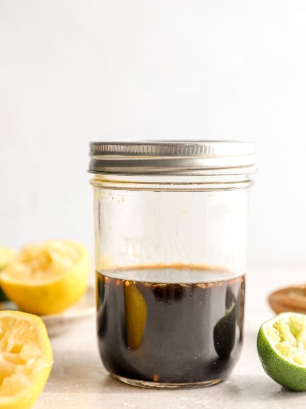 Ponzu sauce in a mason jar with fresh lemon and lime halves on a light surface