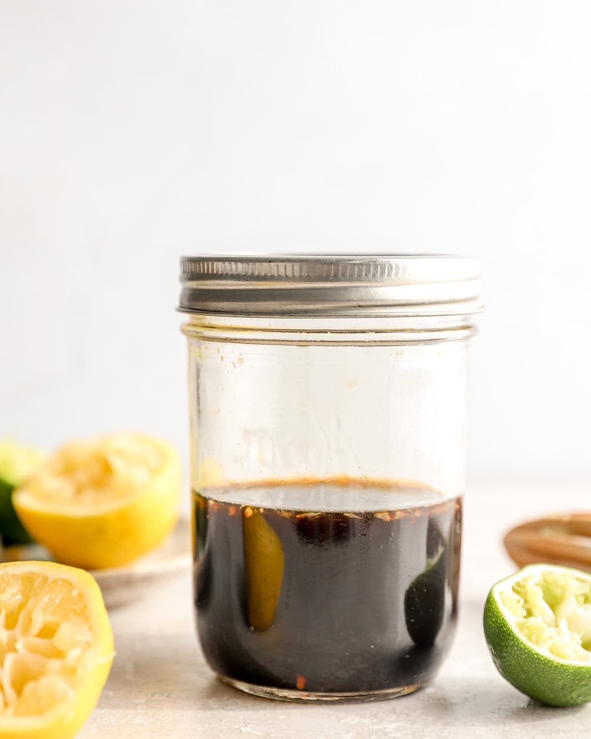 Ponzu sauce in a mason jar with fresh lemon and lime halves on a light surface
