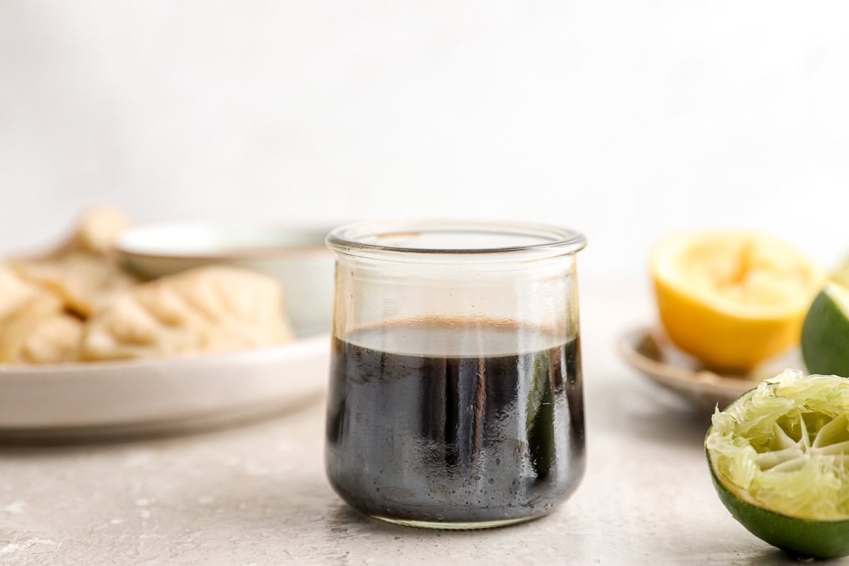 Small glass jar of ponzu sauce with dumplings blurred in the background