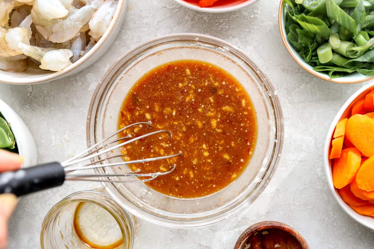 Stir fry sauce being whisked in a glass bowl with garlic and ginger