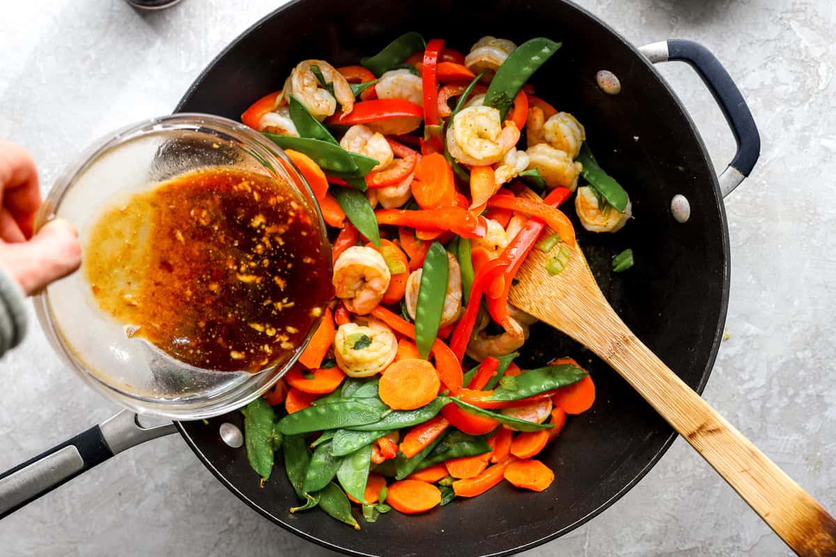 Stir fry sauce being poured over shrimp and vegetables in a skillet