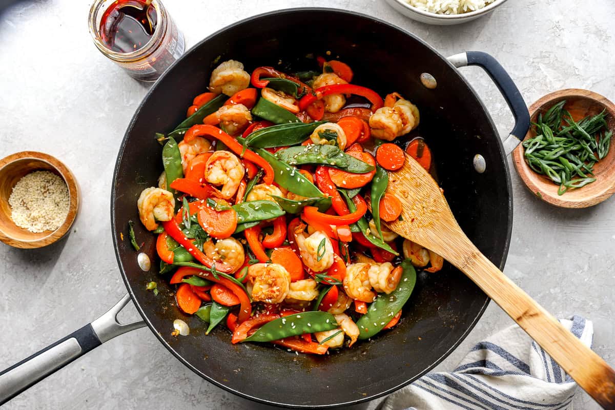 Shrimp stir fry cooking in a pan with vegetables and glossy sauce