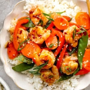 Shrimp stir fry served over white rice with carrots, bell peppers, snow peas, sesame seeds, and green onions