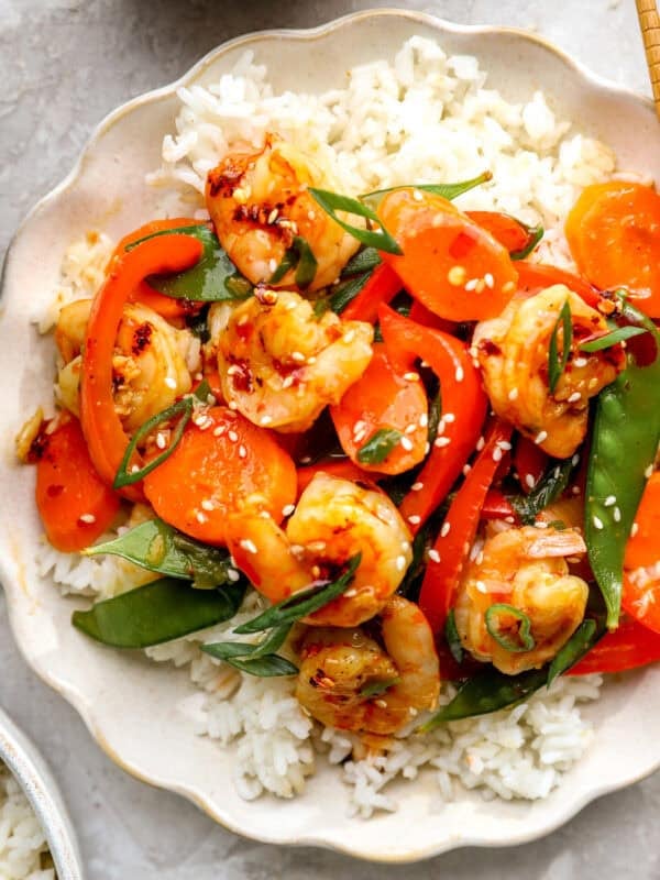 Shrimp stir fry served over white rice with carrots, bell peppers, snow peas, sesame seeds, and green onions