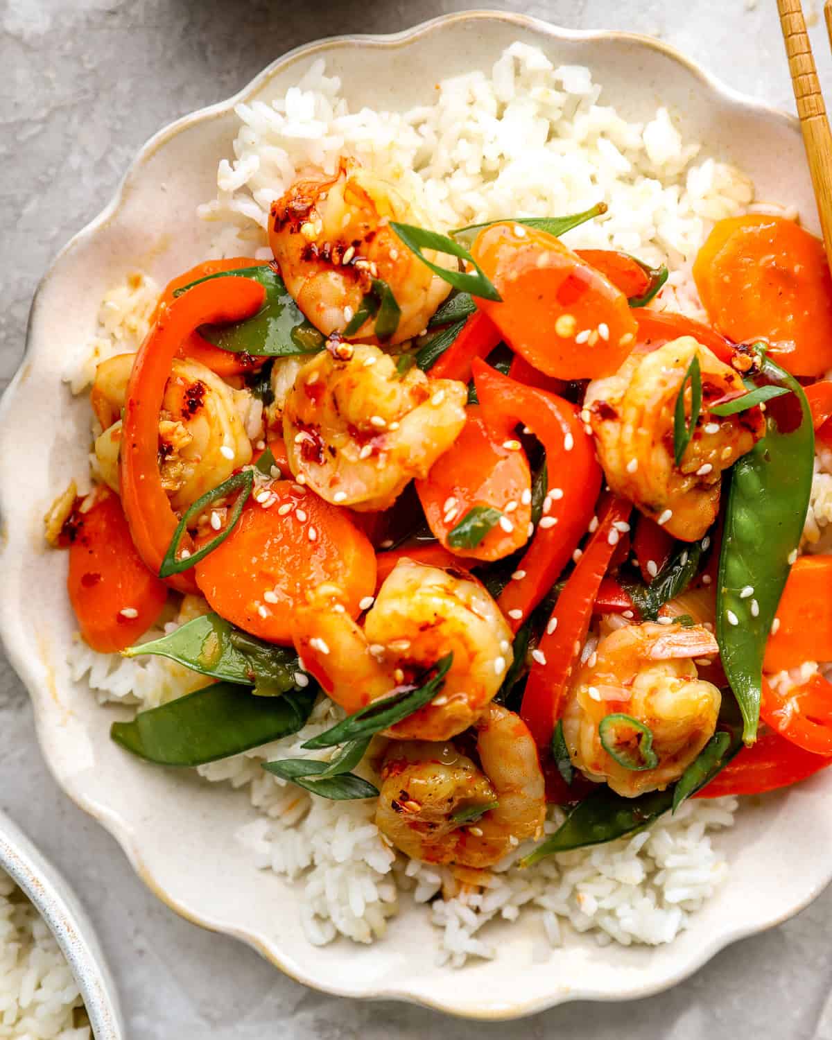 Shrimp stir fry served over white rice with carrots, bell peppers, snow peas, sesame seeds, and green onions