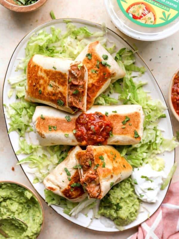 Crispy bean and cheese burritos served with guacamole, salsa, sour cream, and shredded lettuce on a platter.