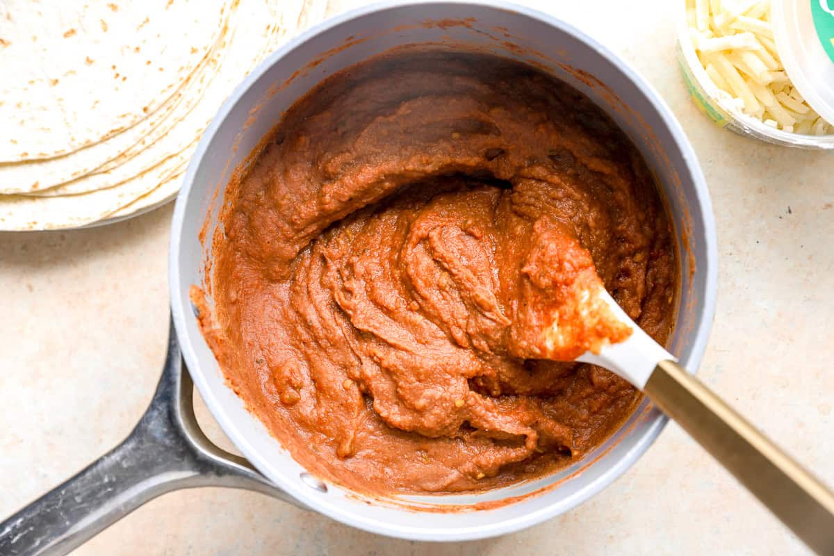 Seasoned refried bean filling mixed in a saucepan until smooth and creamy.