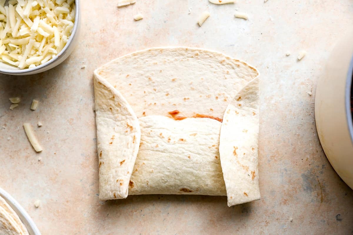 Flour tortilla folded around the bean and cheese filling during the burrito rolling process.