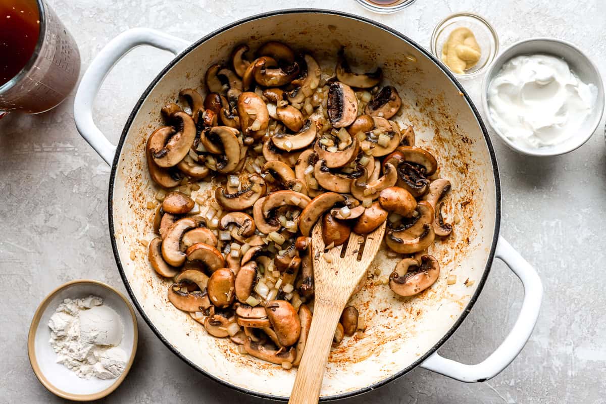 Cremini mushrooms and onions cooking in a skillet for chicken stroganoff sauce