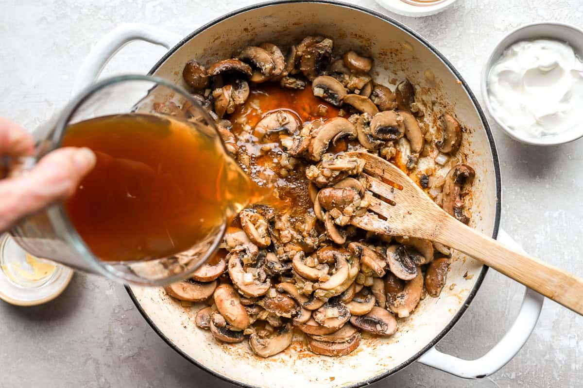 Beef broth being poured into mushrooms and onions for chicken stroganoff sauce