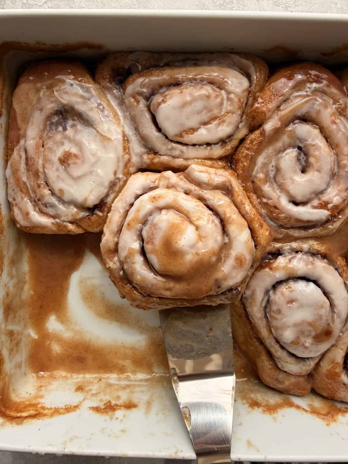 Gooey heavy cream cinnamon rolls topped with icing in a baking dish with caramel sauce underneath.