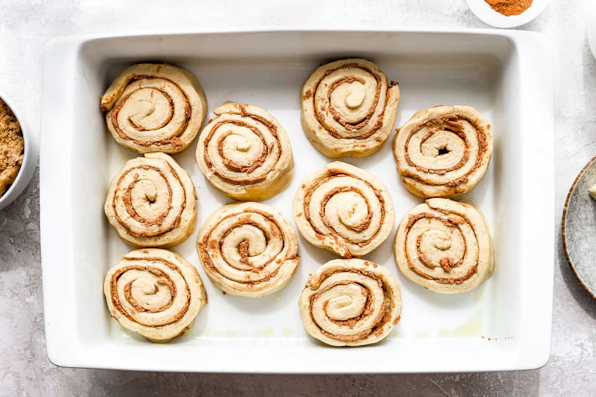Unbaked cinnamon rolls arranged in a baking dish before adding the heavy cream mixture.