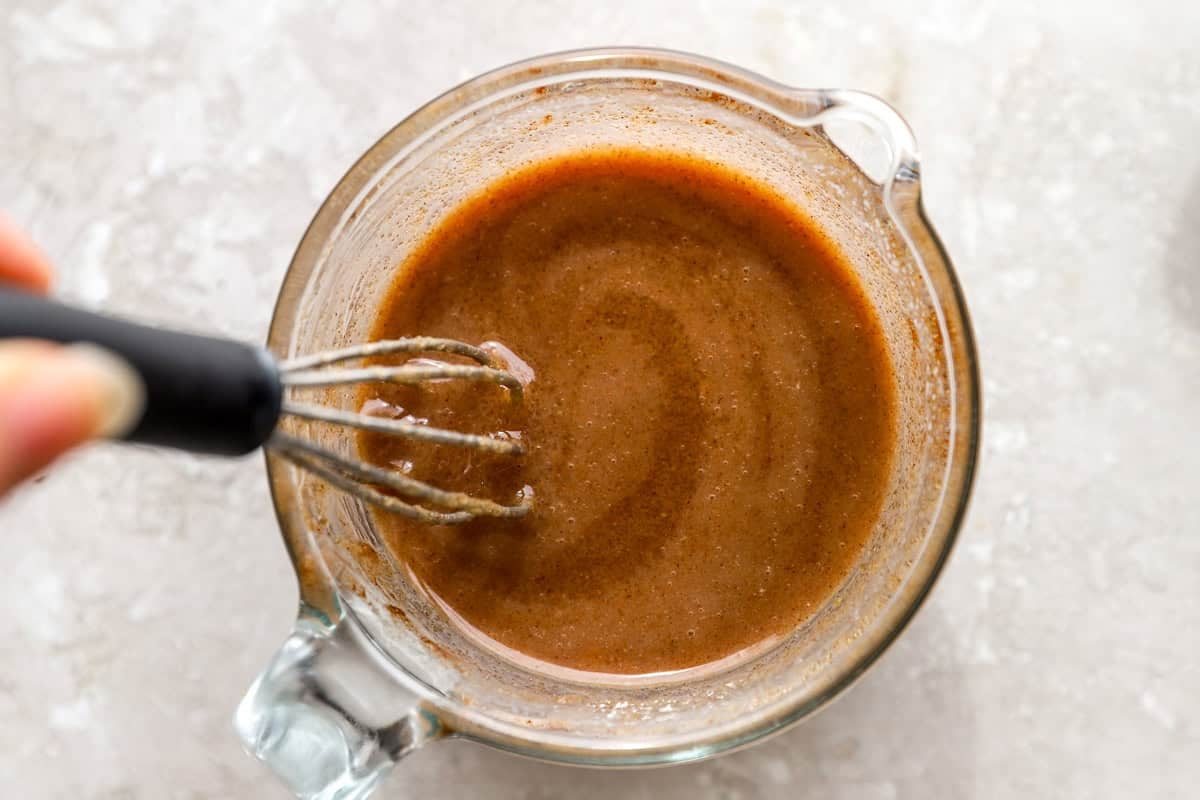 Cinnamon butter and brown sugar mixture being whisked together in a glass measuring cup.