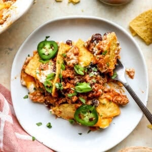Slice of cheesy nacho pie topped with black beans, jalapeños, green onions, and cilantro on a gray plate