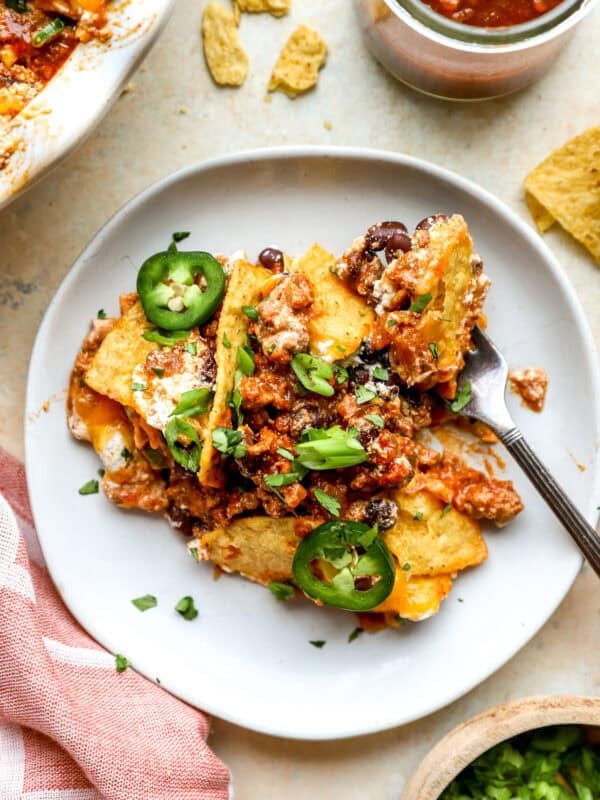 Slice of cheesy nacho pie topped with black beans, jalapeños, green onions, and cilantro on a gray plate