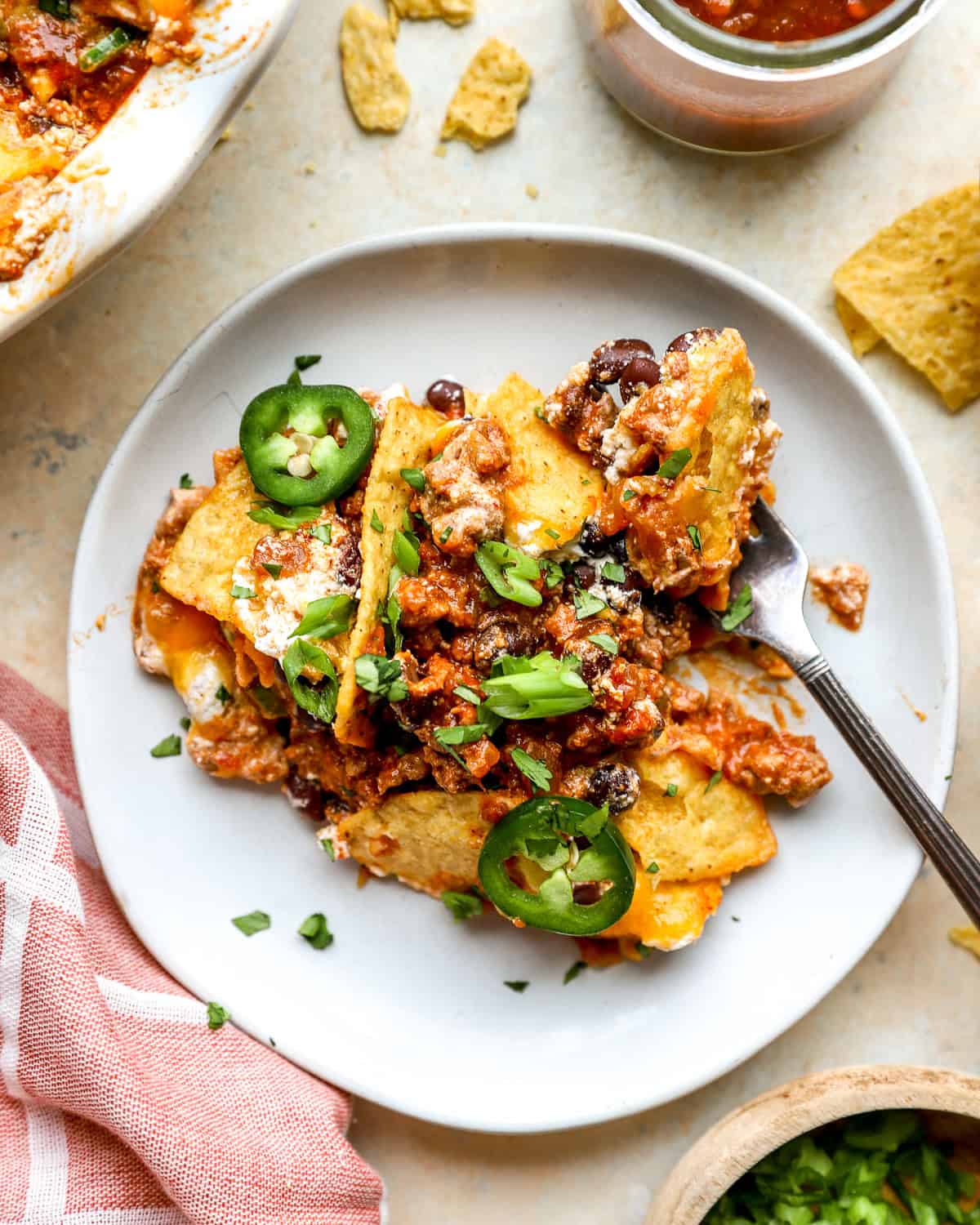 Slice of cheesy nacho pie topped with black beans, jalapeños, green onions, and cilantro on a gray plate