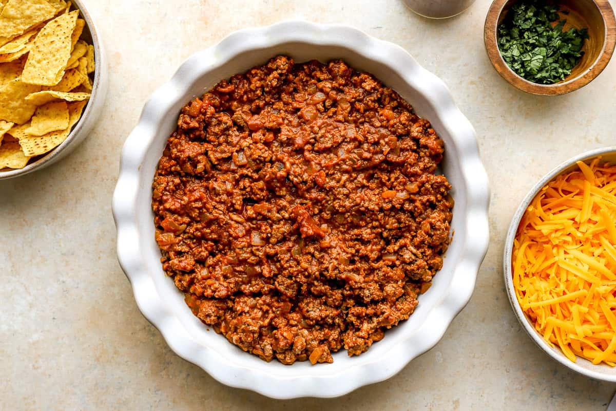 Taco-seasoned ground beef spread into the bottom of a pie dish for nacho pie