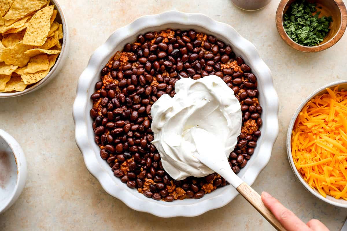 sour cream spread over black beans for nacho pie