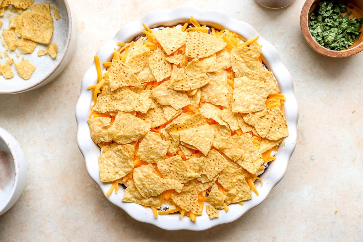 Nacho pie topped with shredded cheddar cheese and crushed tortilla chips before baking