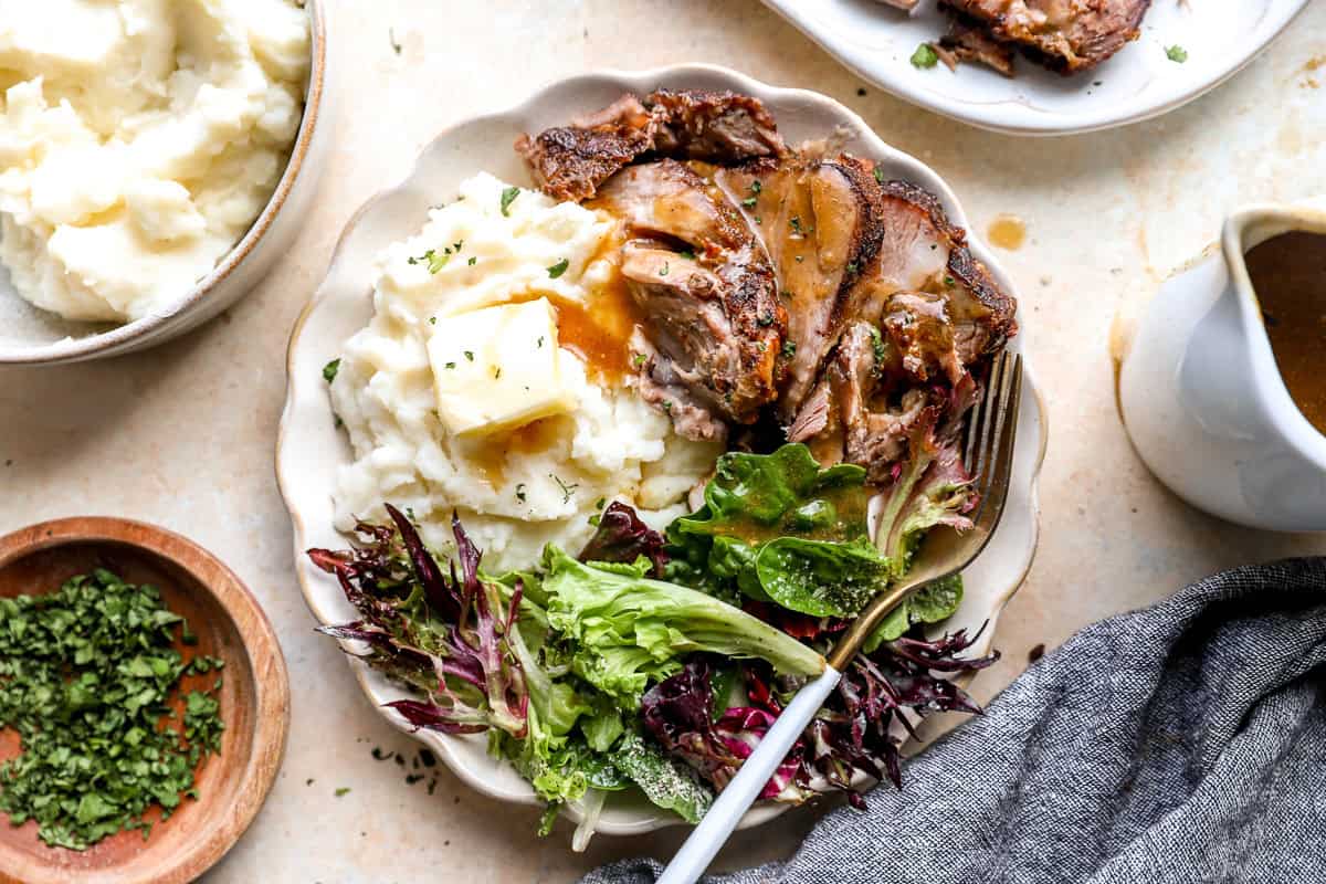 Plate of roasted pork shoulder served with mashed potatoes, salad, and homemade gravy.